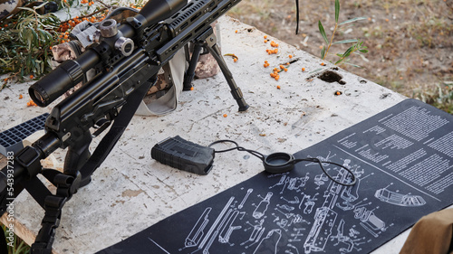 An unfastened clip of an assault rifle against a background of mountain ash and an exploded drawing photo