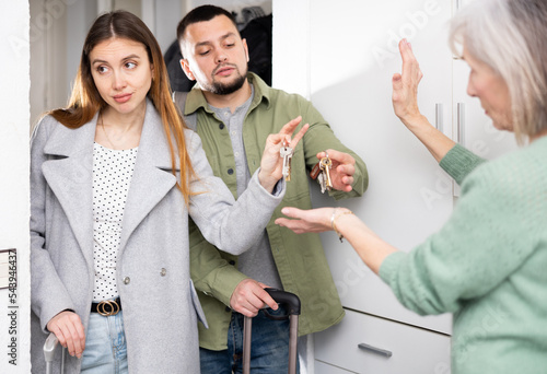 Dissatisfied old woman, owner of apartment, receiving keys from married couple tenants. photo