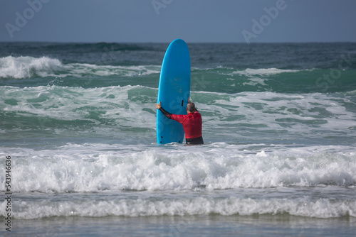 A surfer enters the water at A Lanzada beach with a blue apprentice surfboard