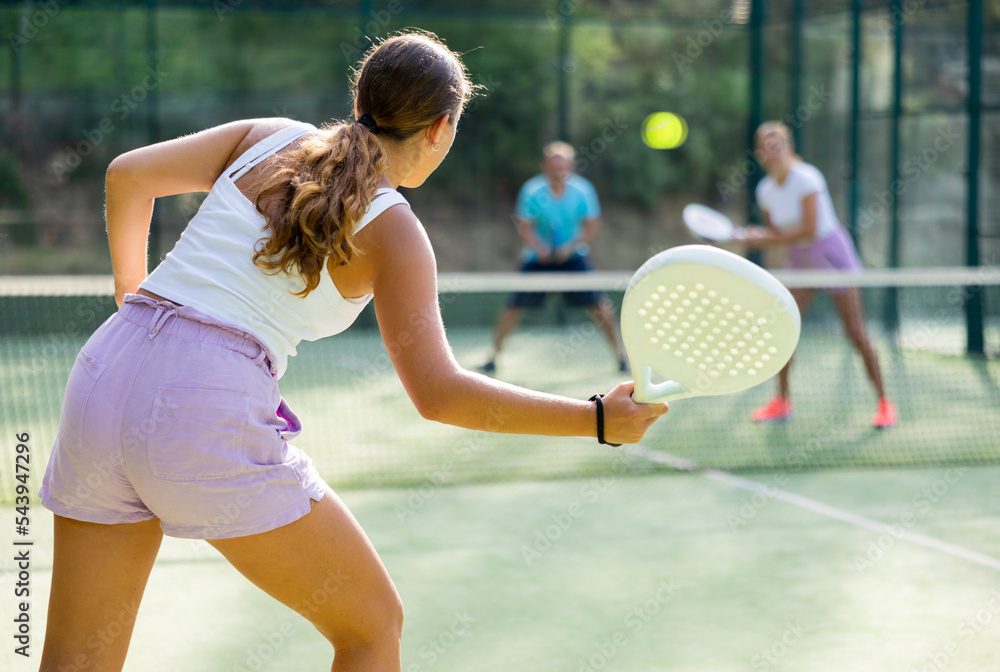 Rear view of young woman in sportswear playing padel tennis on court. Racket sport training outdoors.