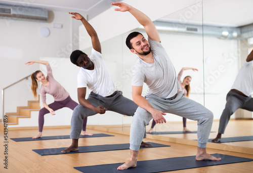 Young bearded man performing stretching during group yoga class in gym. Fitness and Hatha yoga concept..