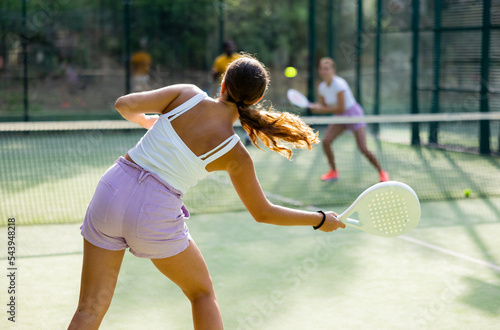 Rear view of woman playing paddle tennis match on outdoor court on blurred background of opponents. Sport and active lifestyle concept © JackF