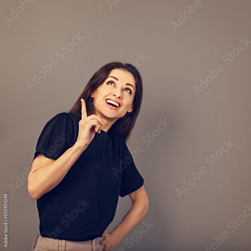 Beautiful positive business happy woman in black casual t- shirt showing up and  demonstrate idea sign by fingers above on empty copy space grey background. Closeup photo