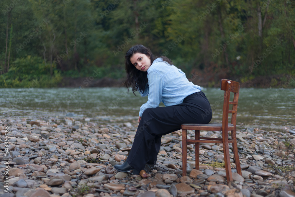 Fototapeta premium A young girl sits on a chair, on the bank of the river, foggy weather