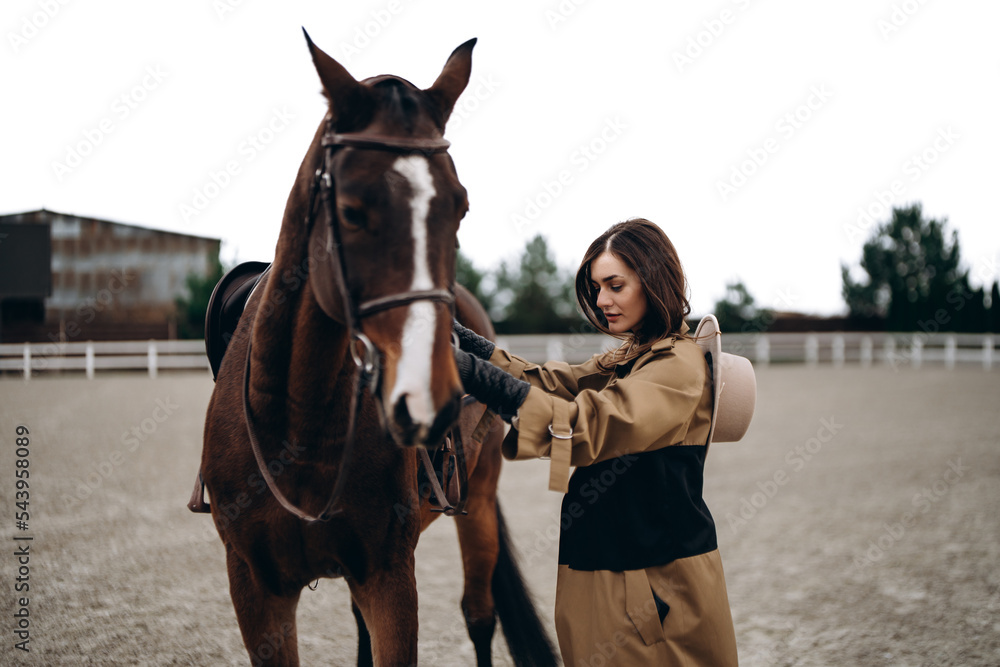 Obraz premium A young woman in a brown coat and hat near a horse.
