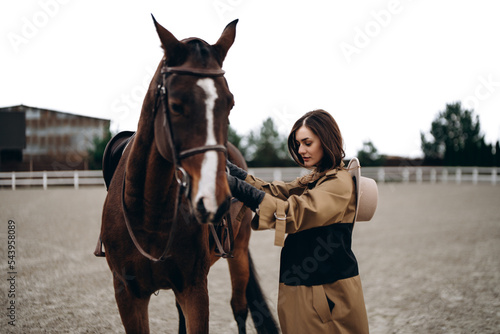 A young woman in a brown coat and hat near a horse. © callisto