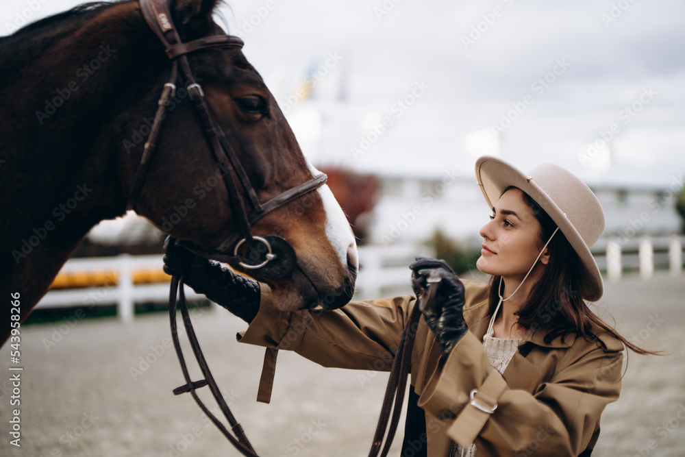 Obraz premium A young woman in a brown coat and hat near a horse.