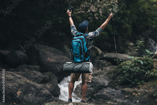 Hikers standing on the rock and raising hands to happy with backpacks and background waterfall in the forest. hiking and adventure concept.