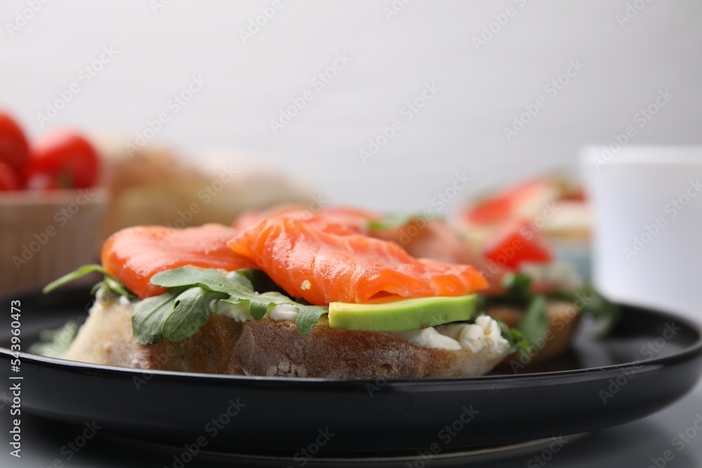 Tasty bruschetta with salmon, arugula and avocado on black plate, closeup Tasty bruschetta with salmon, arugula and avocado on black plate, closeup