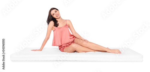 Young woman sitting on soft mattress against white background