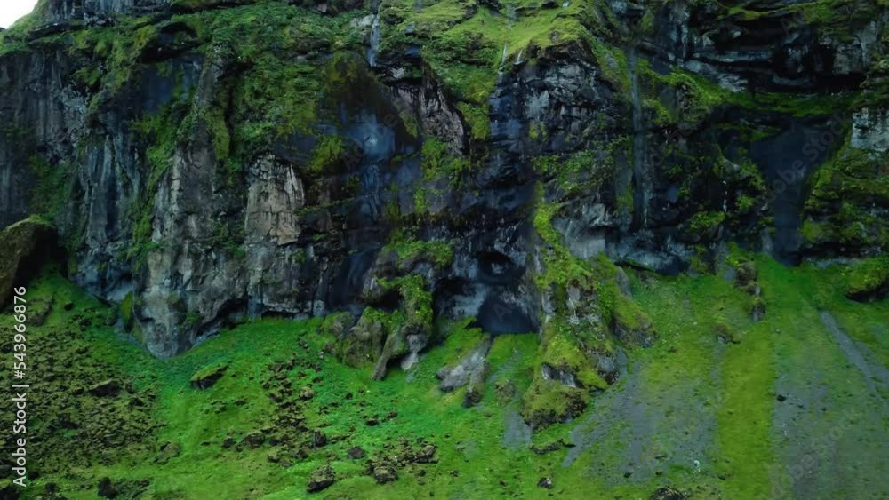 Aerial landscape view of a dark mountain cliff, covered in green moss, in Iceland, with birds flying by Aerial landscape view of a dark mountain cliff, covered in green moss, in Iceland, with birds flying by