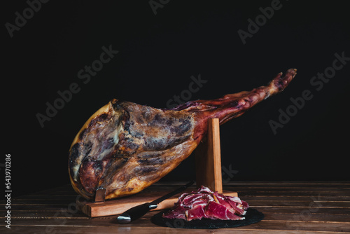 Whole Spanish ham and a plate with sliced ​​ham on a black background