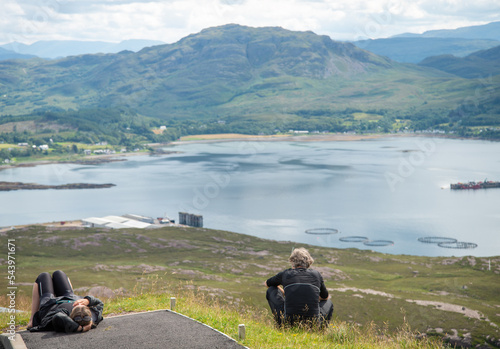 Two cyclists relax,at the summit of Bealach na Ba Viewpoint,mountain pass,overlooking Loch Kishorn. photo