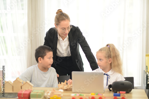 Teacher teaching her young students drawing toys or wood model on the laptop.