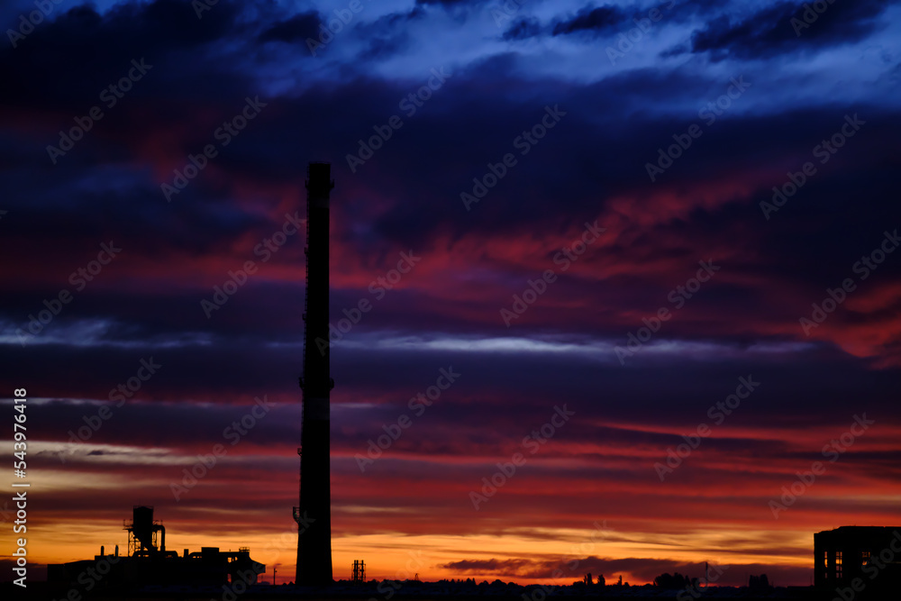 Silhouette of a factory with a large industrial pipe, against the background of an incredible sunset or sunrise sky