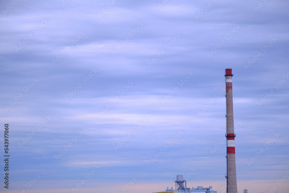 Factory pipe on the background of a beautiful blue sky, with fog or smoke. Evening time