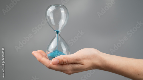 Woman holding an hourglass on a gray background. Close-up.
