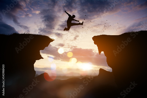 Men jump cliff sun light over silhouette, man is representative of success in the past and gold for the future in 2023