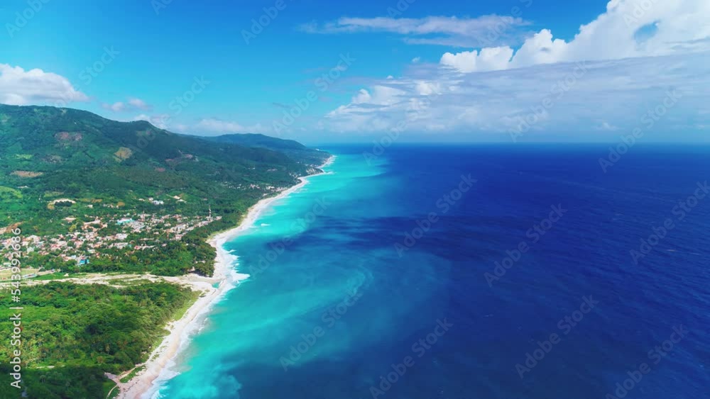 Green peninsula and blue sea. Tropical wildlife landscape of the Dominican Republic on the Caribbean coast from a bird's eye view. White coastline and blue ocean. Bright blue sky with white clouds. Green peninsula and blue sea. Tropical wildlife landscape of the Dominican Republic on the Caribbean coast from a bird's eye view. White coastline and blue ocean. Bright blue sky with white clouds.