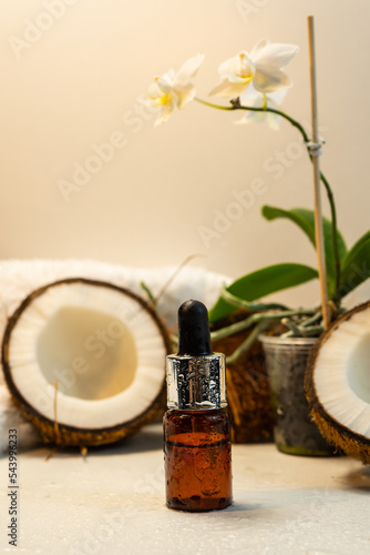 Split coconuts with coconut essential oil.  Coconut serum for the face.   A bottle of whey oil with a pipette on a white-beige background with a coconut shell. Selective focus.   