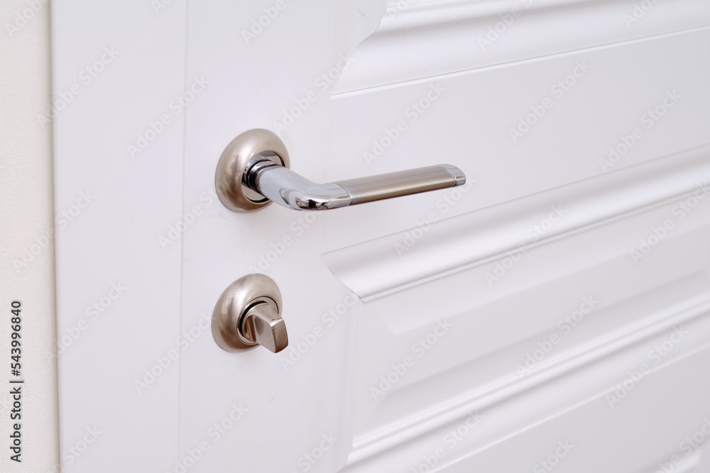 A white door with a lock in the home room and a light switch. Metal door handle in the apartment