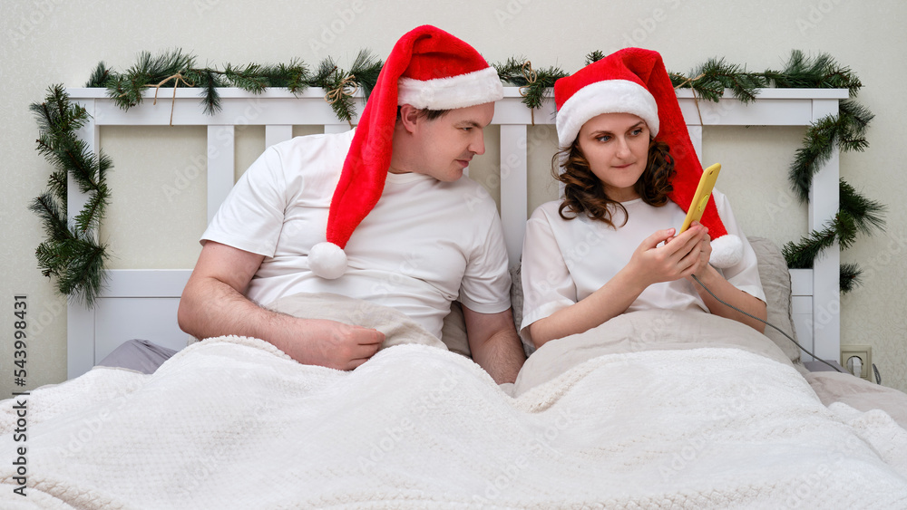 Obraz premium Husband and wife are looking at the phone on a bed decorated for Christmas and New Year in the home bedroom