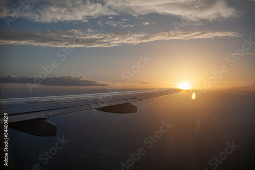 Airplane flight at sunset or dawn. Aircraft's wing and land seen through the illuminator. View from the window of the plane. Airplane, Aircraft. Traveling by air.  © Анатолий Савицкий