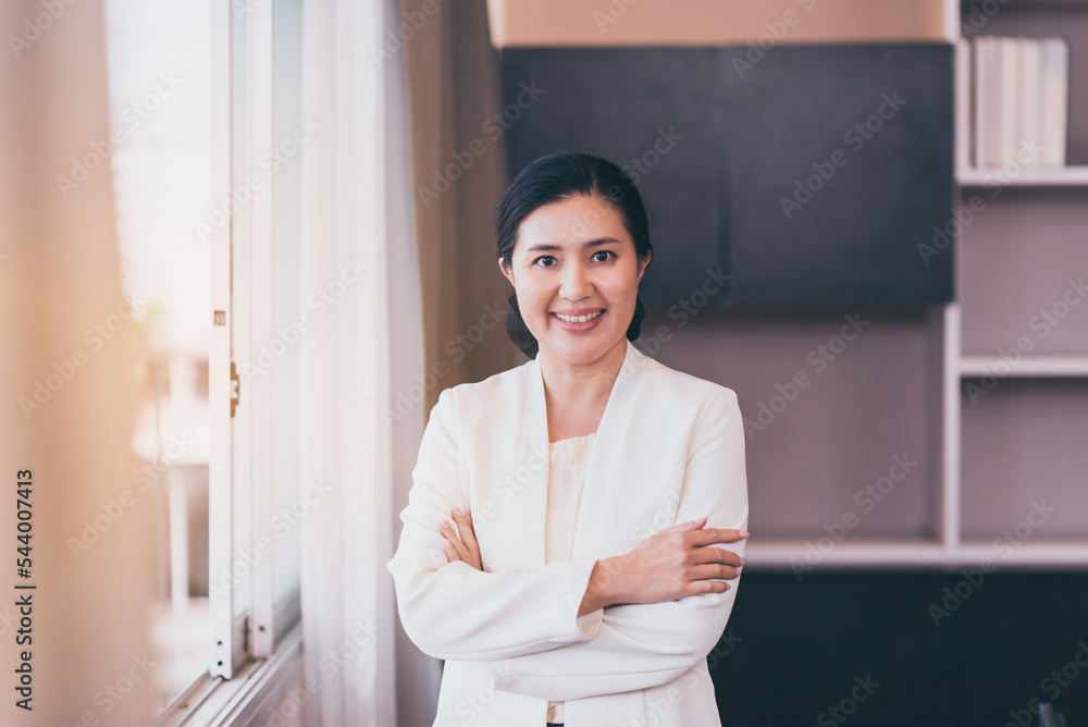 Asian woman boss in white suit cross arms and standing near window at modern office Asian woman boss in white suit cross arms and standing near window at modern office