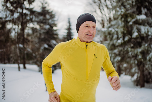 Senior man jogging alone in winter forest.