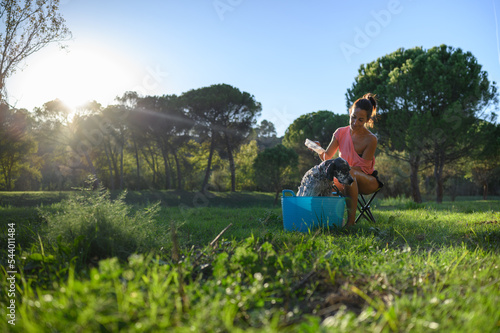 Distant view of middle-aged woman bathing her dog in the garden. Pet care concept.