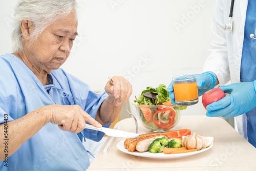Asian senior or elderly old lady woman patient eating breakfast and vegetable healthy food with hope and happy while sitting and hungry on bed in hospital.