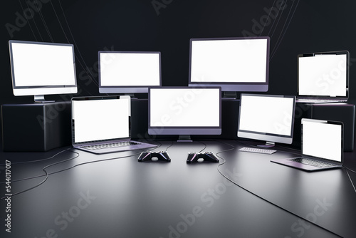 Gaming and streaming concept with blank white glowing modern computer and laptops monitors with space for your text or logo in dark empty room with joysticks on the floor. 3D rendering, mock up