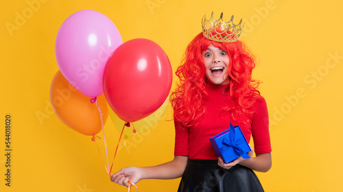 shocked child in crown with present and party balloon on yellow background