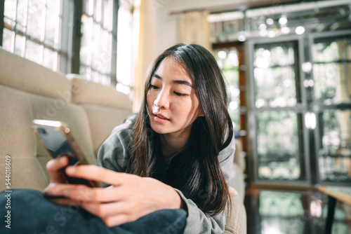 Young adult asian woman relax lying using smartphone for counseling or therapy at home sofa