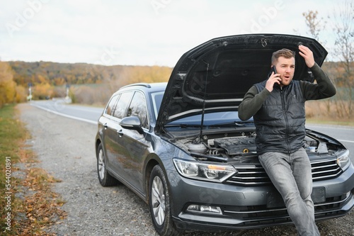 driver trying to figure out how to fix broken down car with red triangle to warn other road users