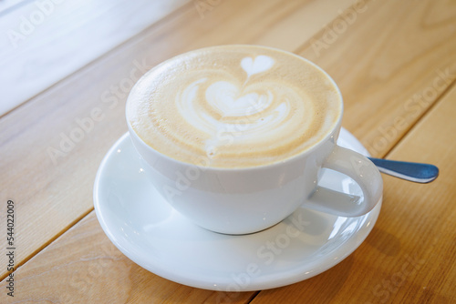 A cup of coffee with a heart-shaped foam close-up on a wooden table.