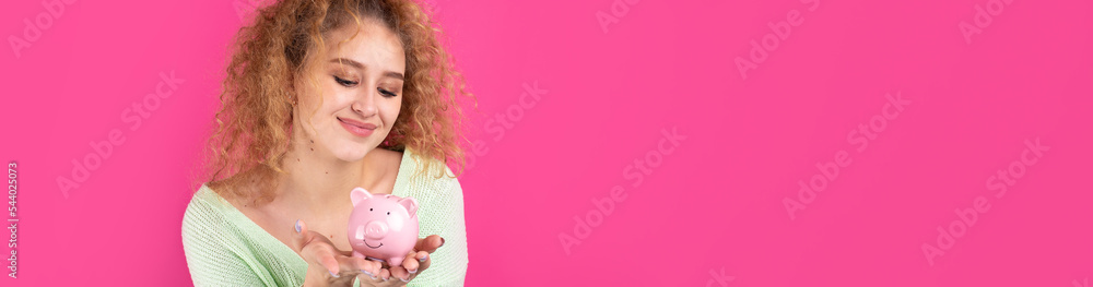 A cute young girl with curly red hair holds a piggy bank, a pink piglet in her hands. The concept of wealth and safety of money. A cute young girl with curly red hair holds a piggy bank, a pink piglet in her hands. The concept of wealth and safety of money.