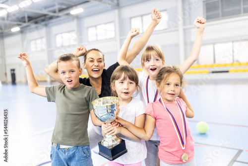 Teacher cheering with students holding trophy at school sports court photo