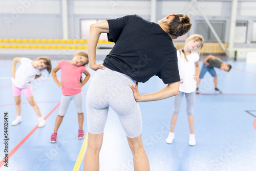 Instructor with hand on hip doing exercise with students at school sports court photo