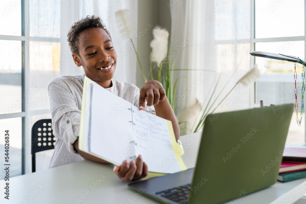 Smiling boy showing notes on video call through laptop at home Smiling boy showing notes on video call through laptop at home
