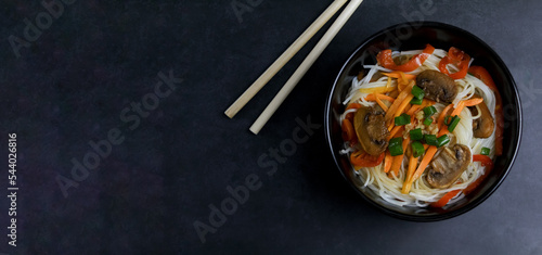 Asian funchose noodles with vegetables, mushrooms and carrots, copy space, dark background 