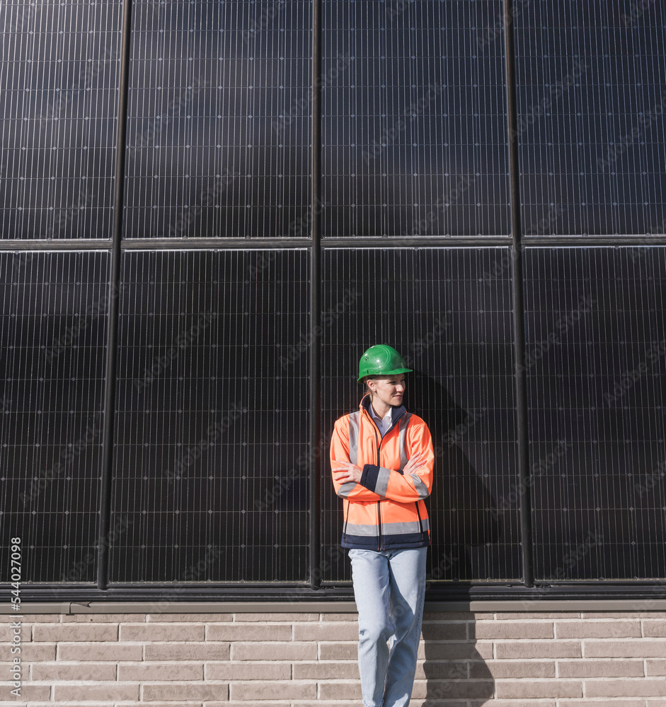 Contemplative female engineer with arms crossed leaning on solar panels Contemplative female engineer with arms crossed leaning on solar panels