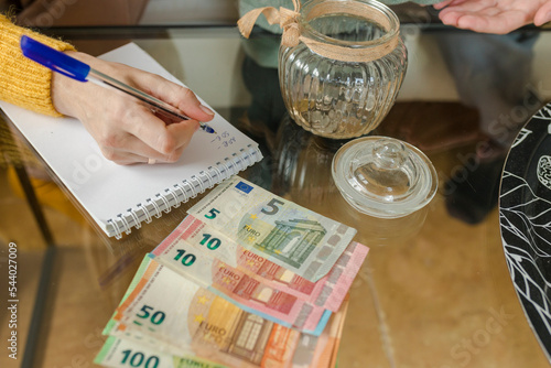 Hand of woman writing on note pad and counting currency at home photo