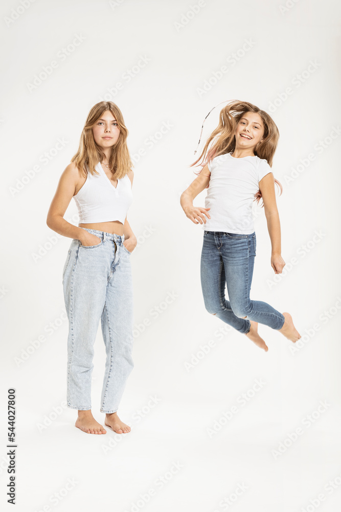 Confident teenage girl by sister jumping against white background Confident teenage girl by sister jumping against white background