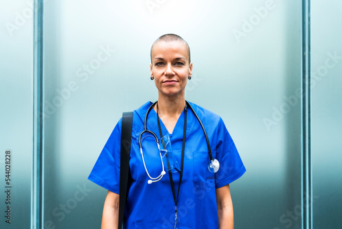 Mature female nurse with stethoscope in front of wall