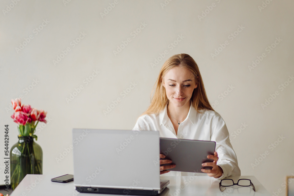 Photo of a cheerful young blonde business woman in office indoors work with laptop and mobile phone. Photo of a cheerful young blonde business woman in office indoors work with laptop and mobile phone.