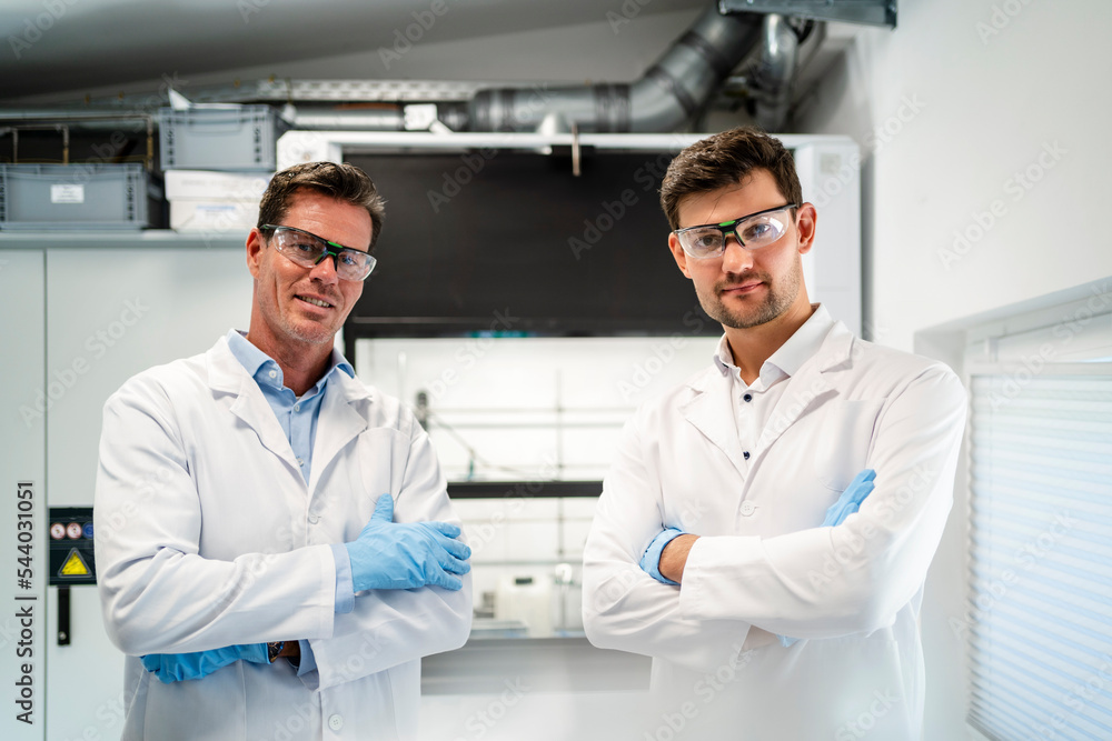 Scientists in lab coats standing with arms crossed in laboratory Scientists in lab coats standing with arms crossed in laboratory