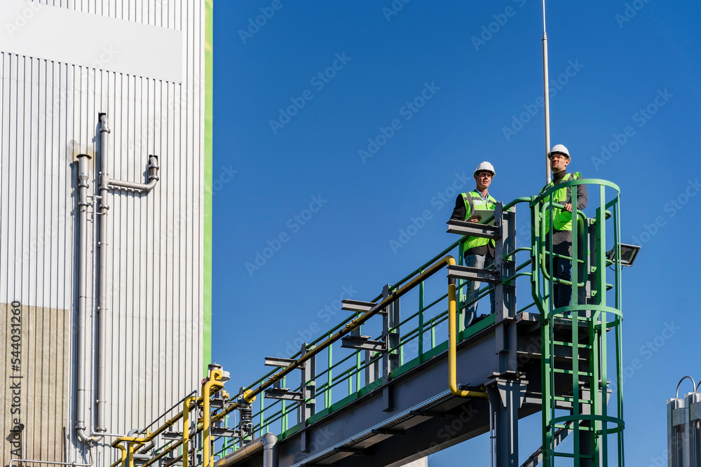 Engineers examining and standing on bridge at recycling plant on sunny day Engineers examining and standing on bridge at recycling plant on sunny day