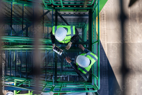 Engineers wearing hardhats discussing with tablet PC at industrial plant