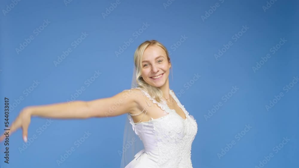 Young beautiful blonde smiling in a wedding white dress and veil on a blue background. The girl looks into the camera. Wedding Young beautiful blonde smiling in a wedding white dress and veil on a blue background. The girl looks into the camera. Wedding